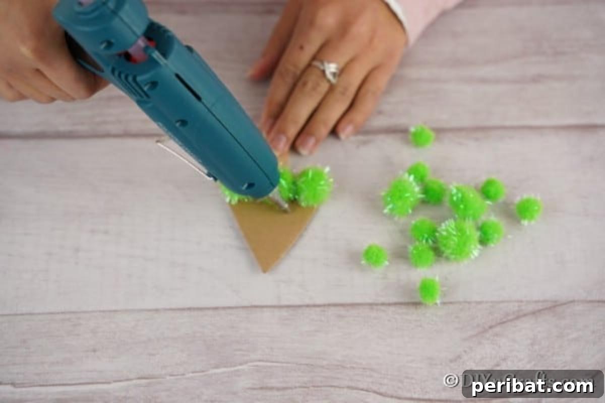 Whimsical Pom Pom Christmas Tree Decoration 8 Hands gluing green pom poms onto the cardboard Christmas tree craft base