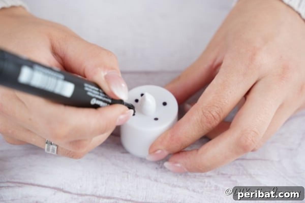 Drawing a simple face, including eyes and a mouth, onto the battery-operated tealight candle to create the snowman Christmas candle