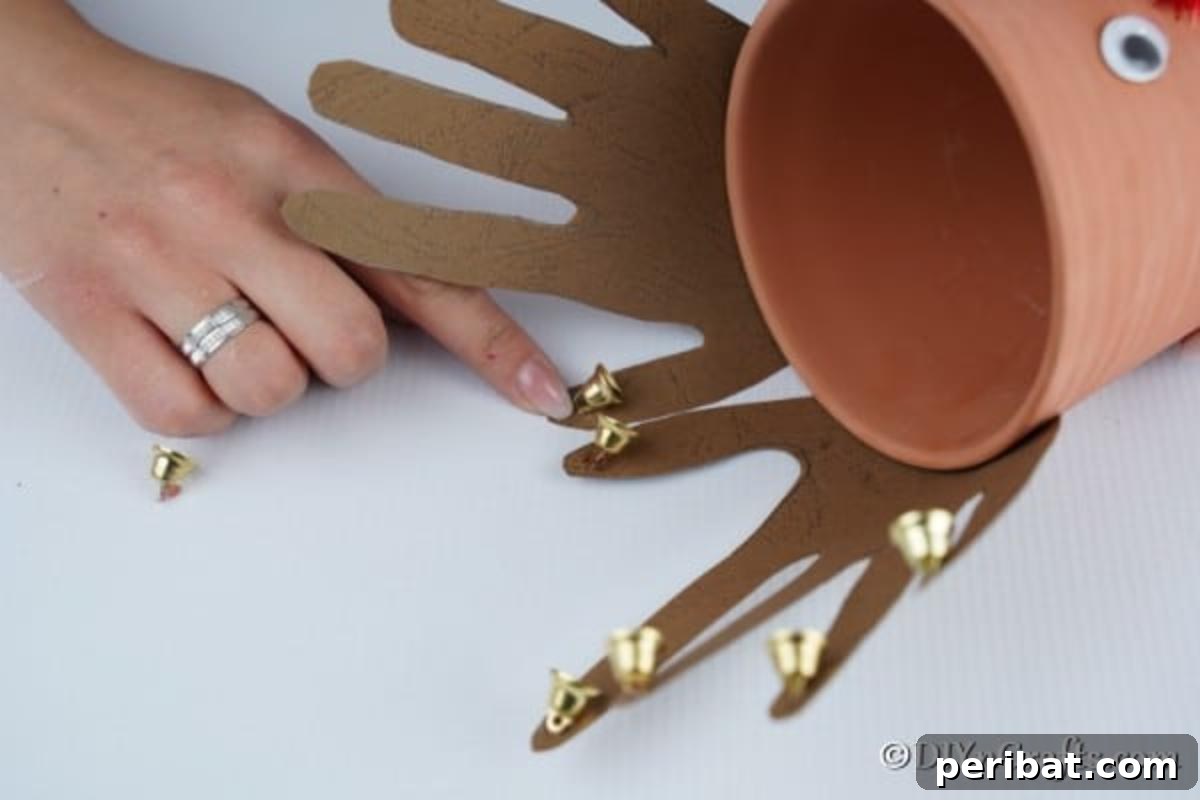 Whimsical Clay Pot Reindeer Christmas Creations 14 Hands meticulously gluing small jingle bells onto the intricate cardboard horns of a large reindeer flower pot decoration, adding a charming auditory and visual detail to the Christmas craft.