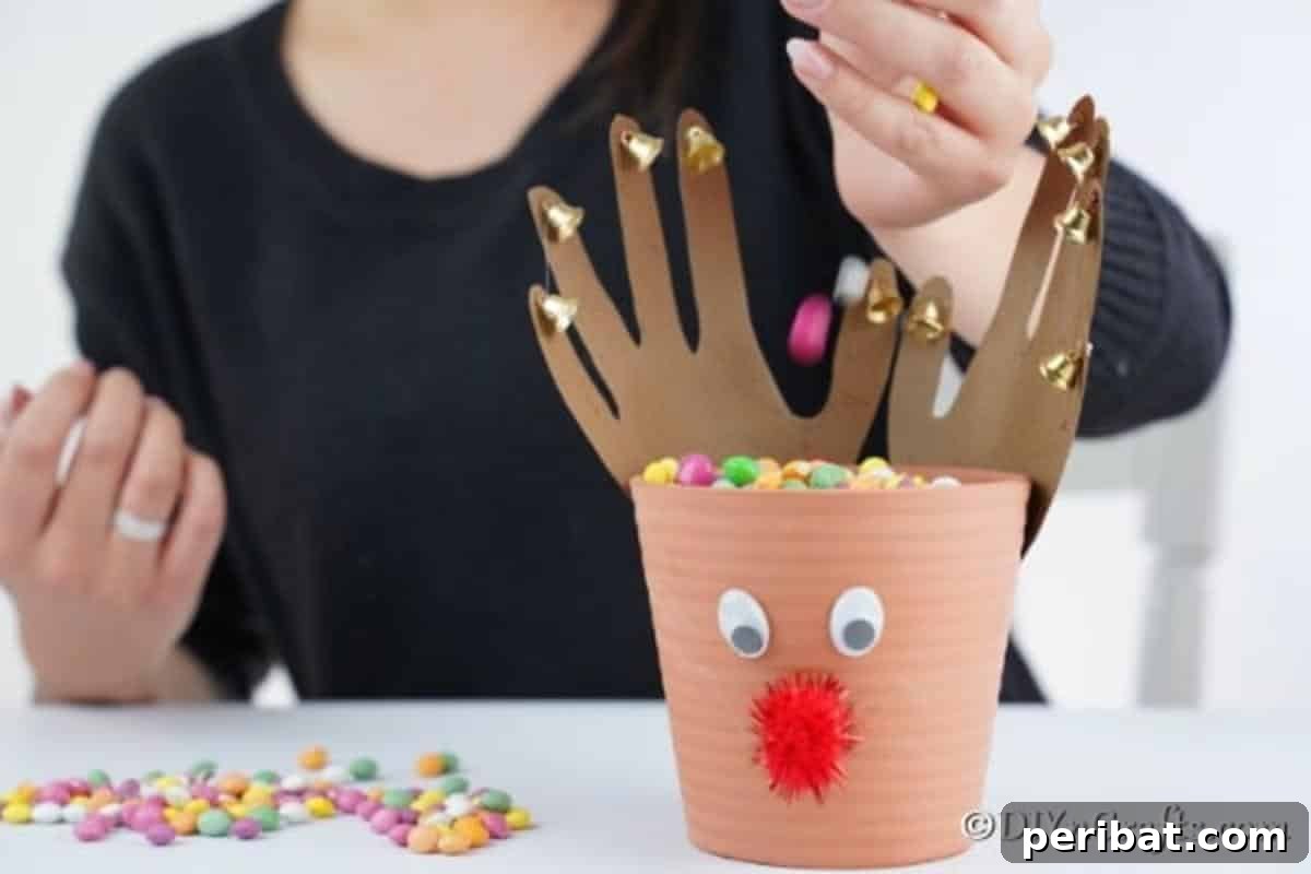 Whimsical Clay Pot Reindeer Christmas Creations 15 Close-up shot of an adult hand gently pouring a cascade of vibrant, wrapped candy pieces into the open top of a large, handmade reindeer flower pot, preparing it as a festive treat holder.