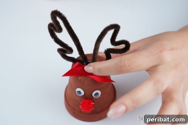 Whimsical Clay Pot Reindeer Christmas Creations 20 Gluing the bow and horns to the top of a reindeer christmas decor piece