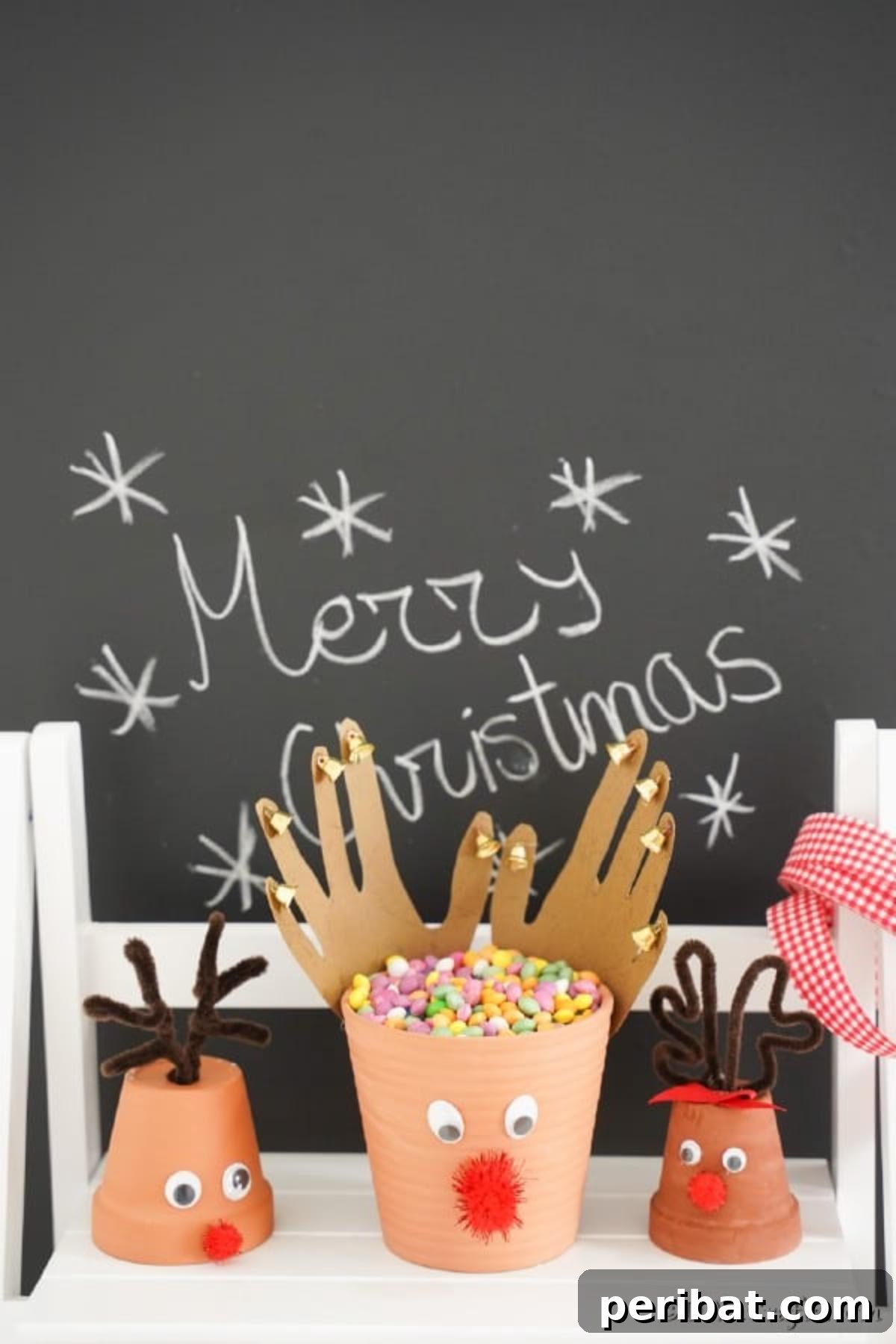Whimsical Clay Pot Reindeer Christmas Creations 4 A trio of charming flower pot reindeers, each with unique antlers and festive bows, positioned neatly on a white shelf against a backdrop of a rustic Christmas chalkboard sign, embodying cozy holiday aesthetics.
