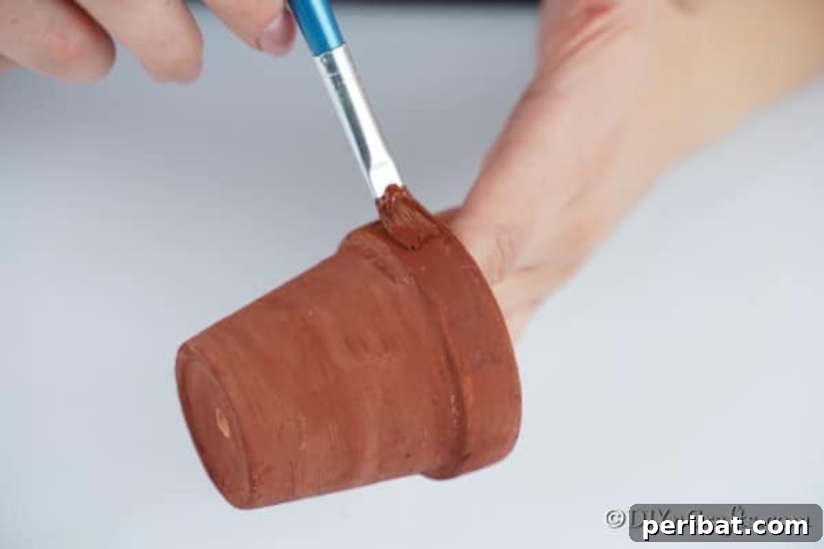 Whimsical Clay Pot Reindeer Christmas Creations 7 A close-up view of hands meticulously painting terra cotta pots with brown paint, preparing them for transformation into charming reindeer Christmas decorations, highlighting the initial crafting stage.