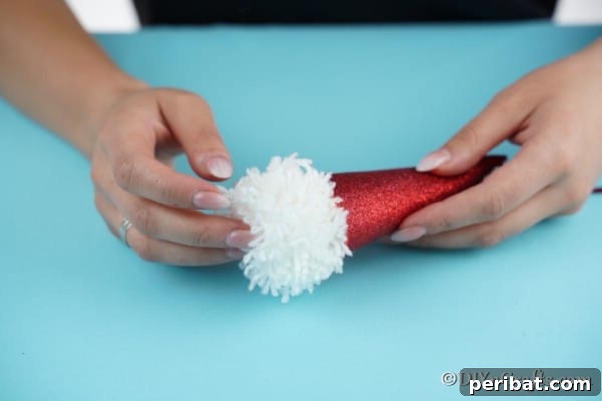 Cozy Pom-Pom Gnomes: Whimsical Holiday Tree Charms 12 Gluing the white pom pom in place on cone to create a gnome face