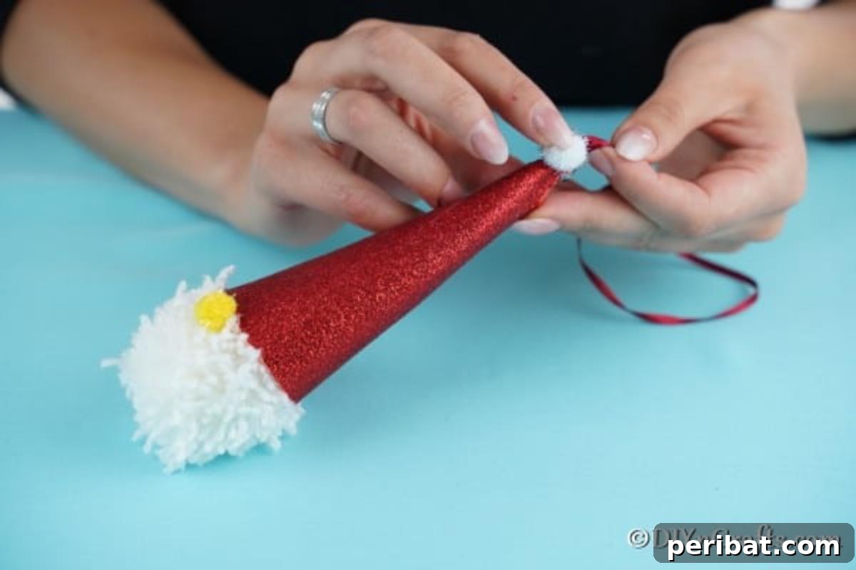Cozy Pom-Pom Gnomes: Whimsical Holiday Tree Charms 13 Adding final touches to Christmas gnome with pom poms for a nose and at the top of santas hat
