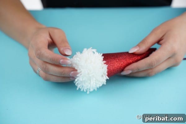 Cozy Pom-Pom Gnomes: Whimsical Holiday Tree Charms 22 Gluing the white pom pom in place on cone to create a gnome face