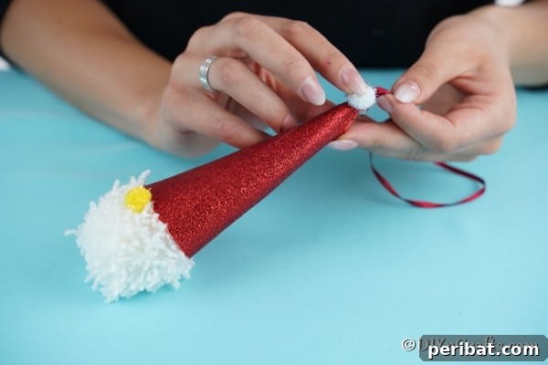 Cozy Pom-Pom Gnomes: Whimsical Holiday Tree Charms 23 Adding final touches to Christmas gnome with pom poms for a nose and at the top of santas hat