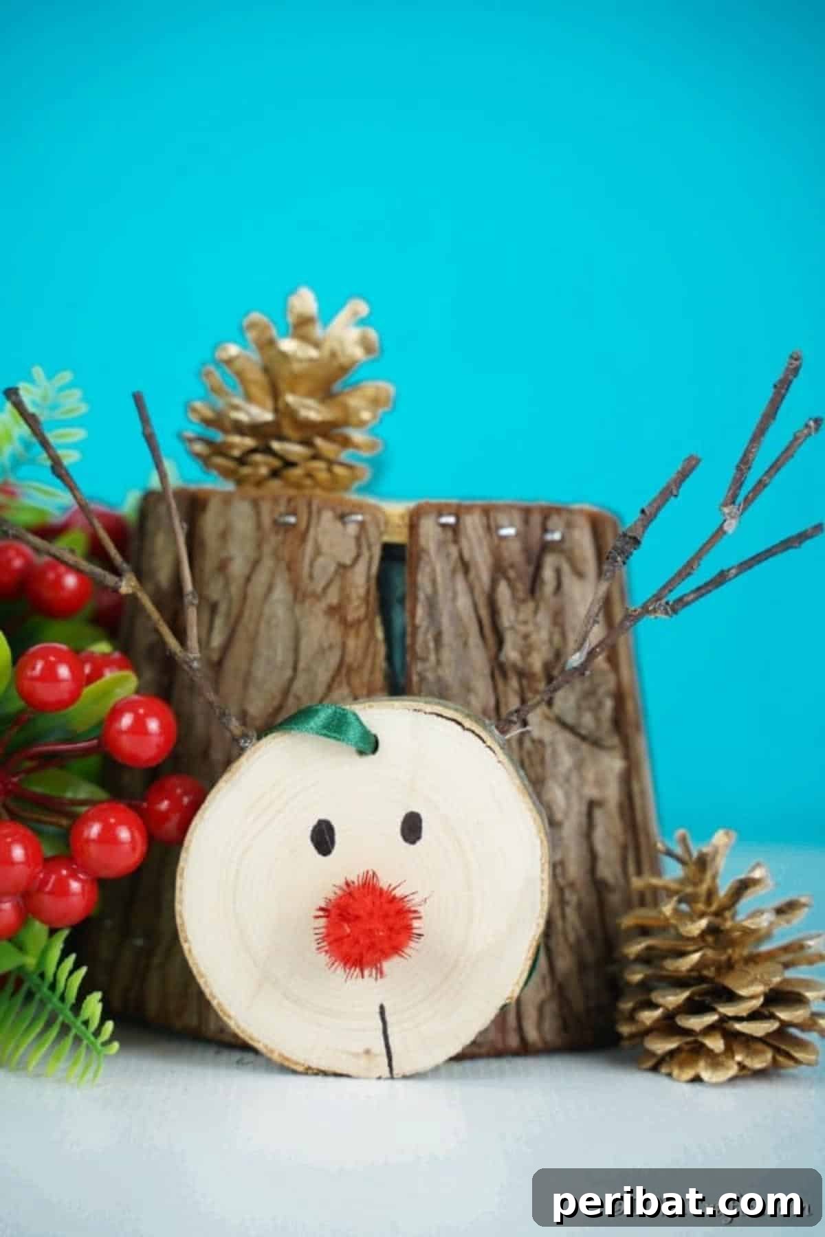 A wood slice reindeer ornament leaning against a tree trunk segment, surrounded by festive holiday decorations.