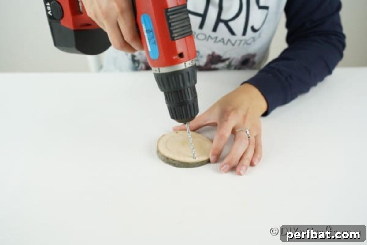 Drilling a small hole in the top of a wood slice to prepare it for hanging on a Christmas tree.