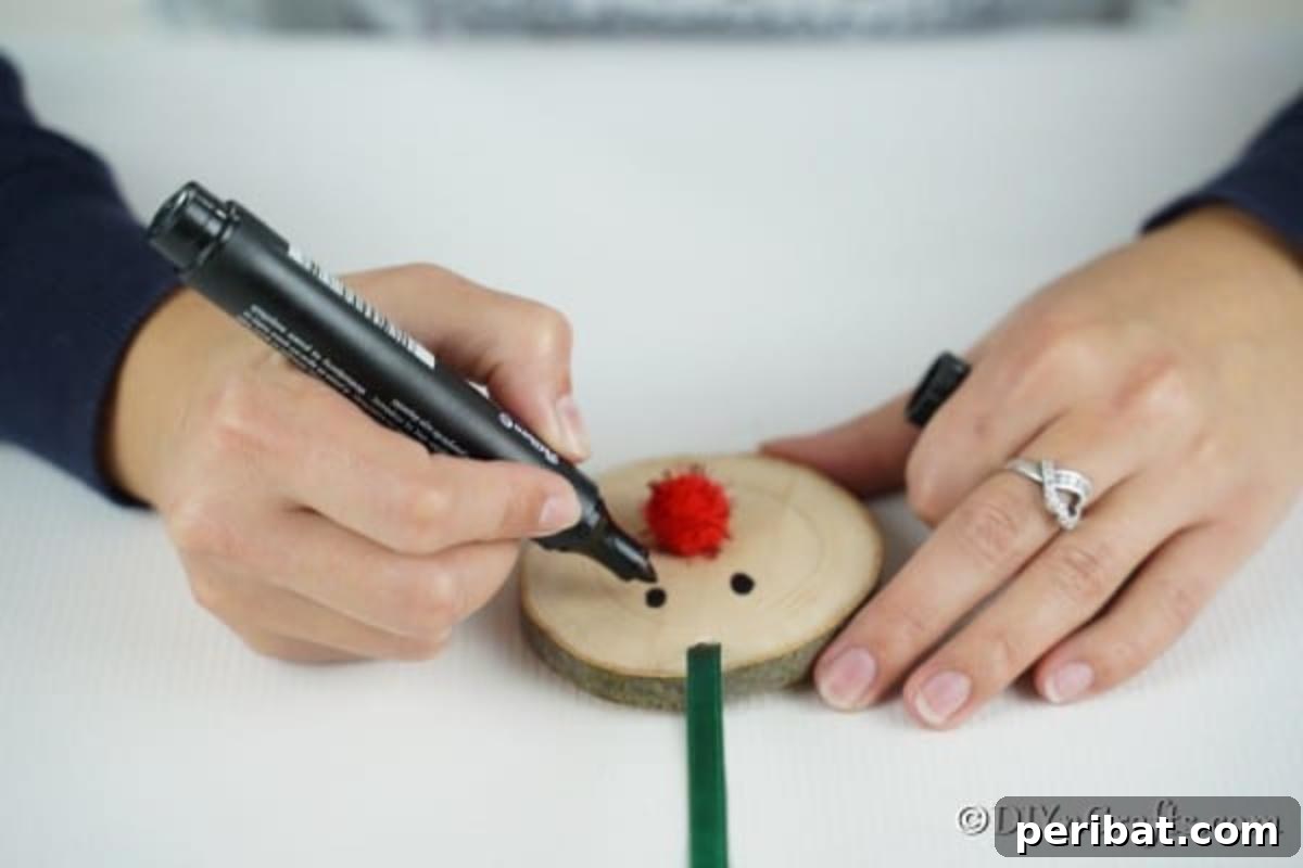 Adding facial features (eyes and mouth) to the wood slice using a black marker for the reindeer ornament.