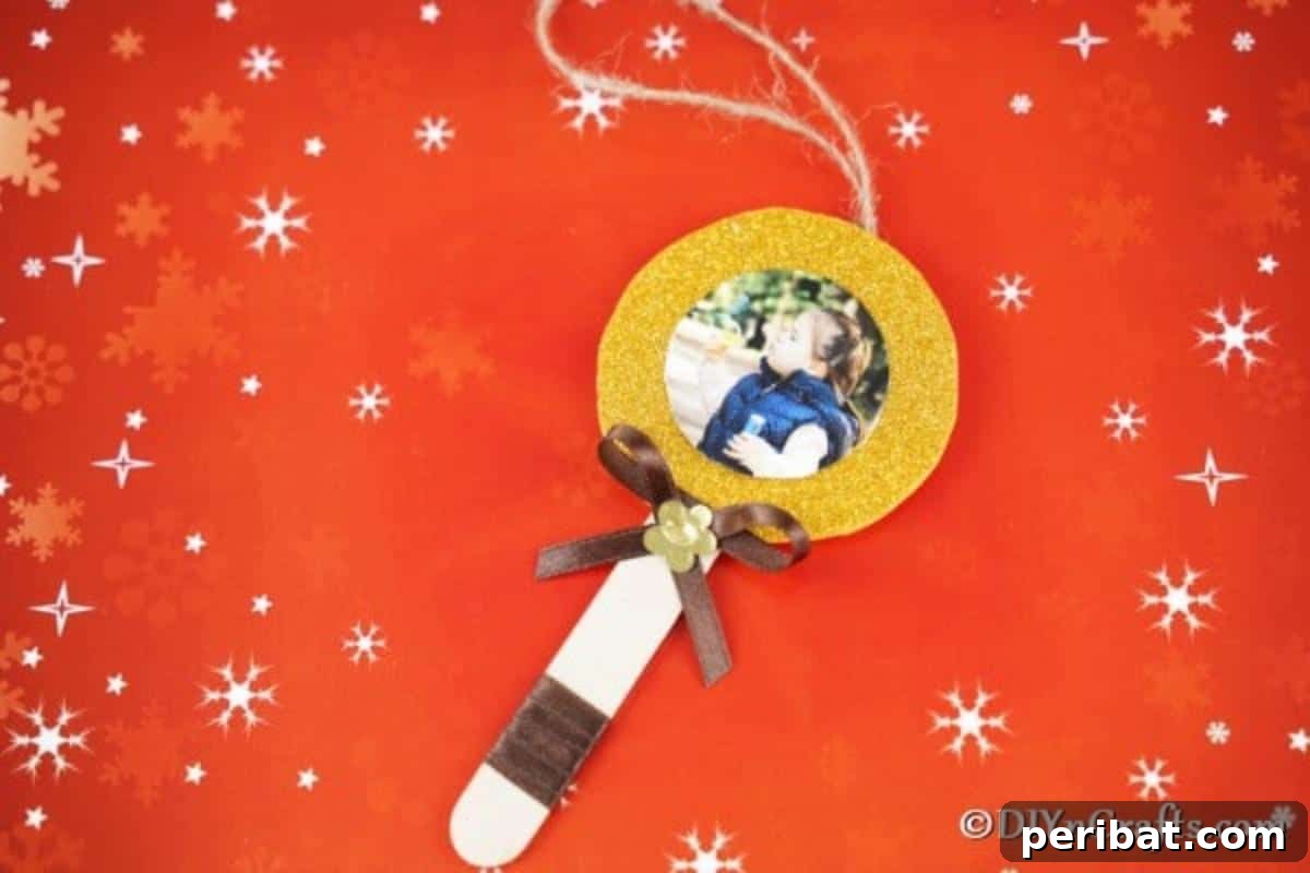 Sweet Memories: Craft Stick Photo Lollipops 3 A sparkling craft stick lollipop photo ornament resting on a festive orange paper adorned with stars, showcasing its vibrant glitter border and personal touch.