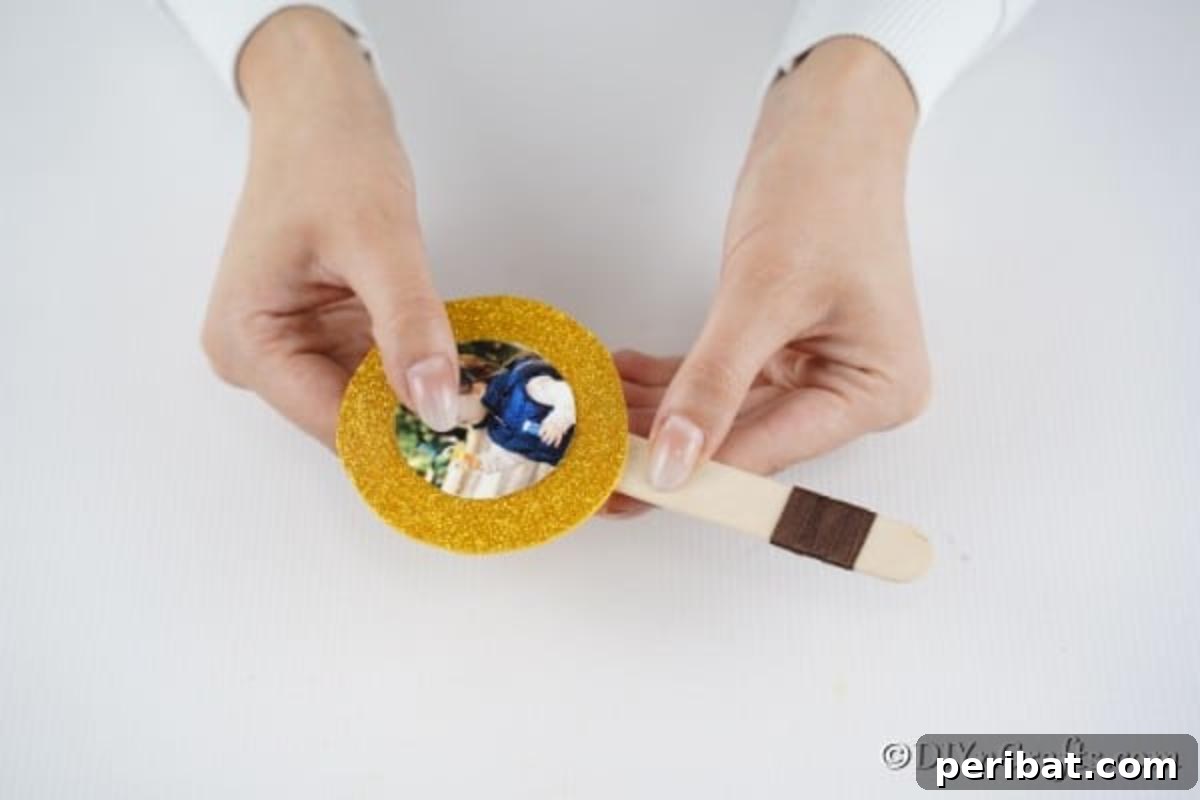 Sweet Memories: Craft Stick Photo Lollipops 10 Securing the glitter paper circle, with the photo, to the craft stick using hot glue, forming the main structure of the lollipop ornament.