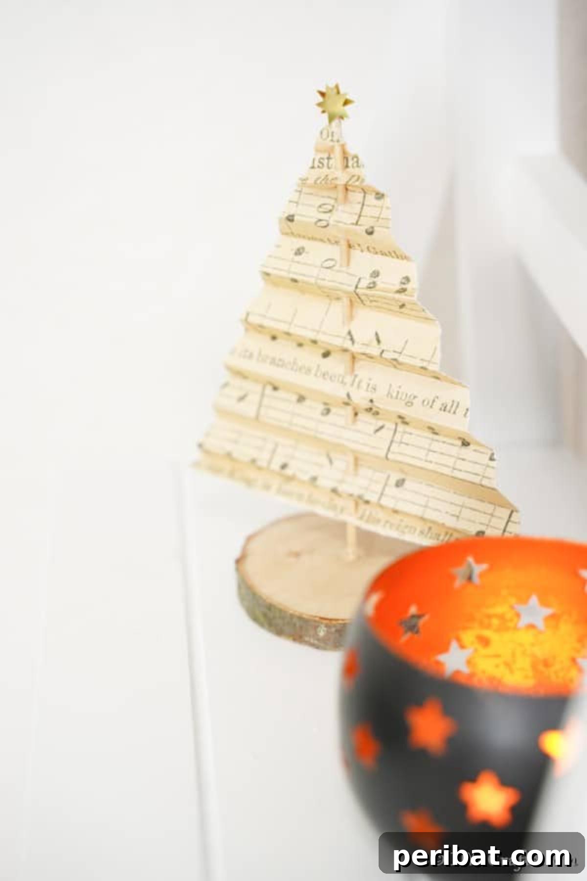 Melody-Folded Christmas Tree 14 A charming sheet music paper Christmas tree displayed gracefully on a mantle, alongside a small, glowing candle, embodying festive tranquility.