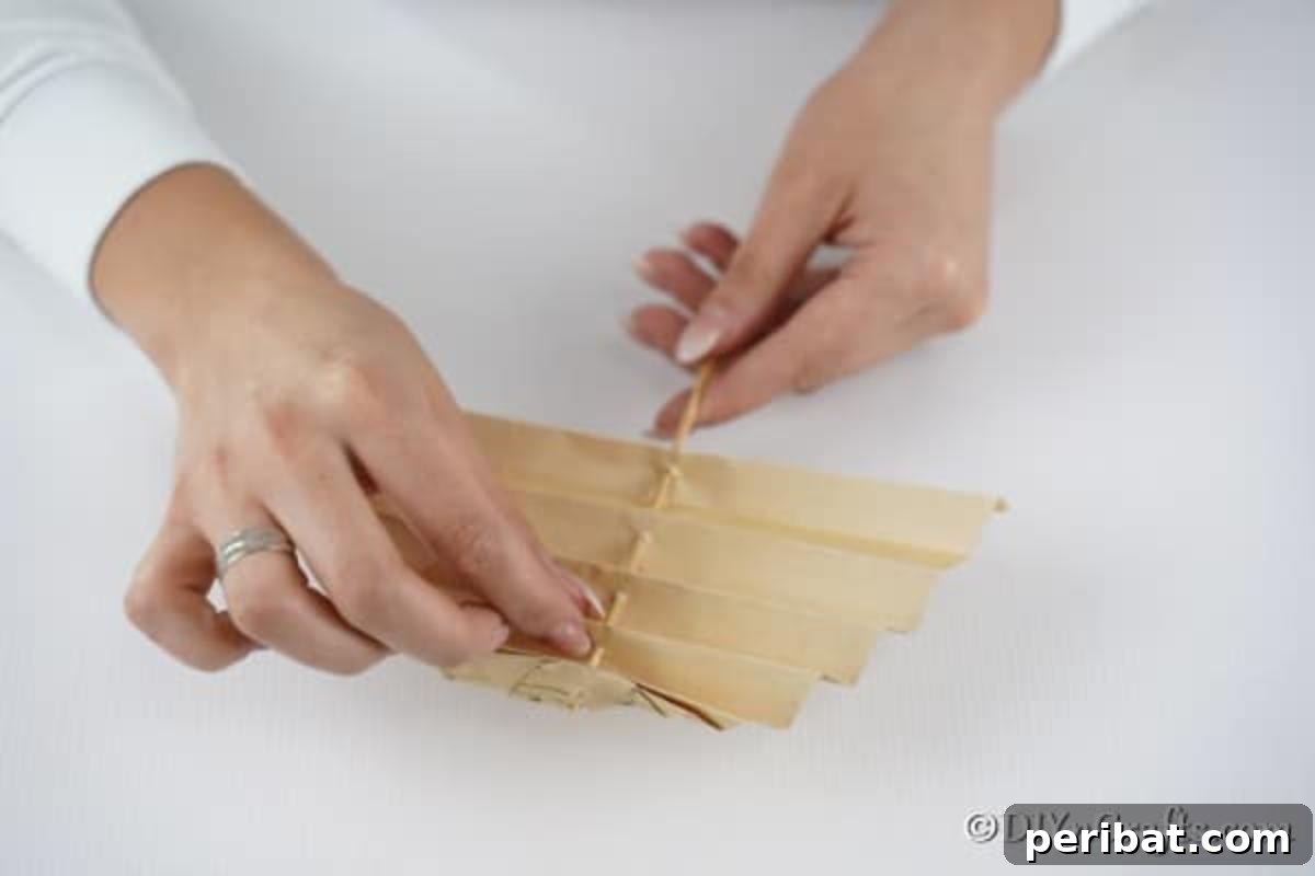 Melody-Folded Christmas Tree 10 Gently pushing the dowel rod through the prepared paper Christmas tree, demonstrating the assembly process.