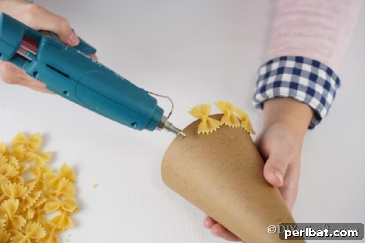 Creative Pasta Christmas Ornaments 11 Carefully adding bow tie pasta to the cone base, layer by layer, to construct the textured body of the Christmas tree.