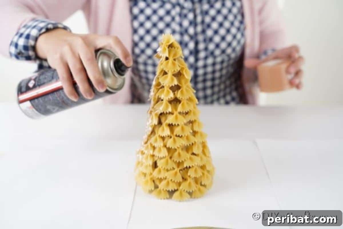 Creative Pasta Christmas Ornaments 13 Vibrantly spray painting a pasta Christmas tree with shimmering gold paint, bringing it to life with a festive and elegant finish.