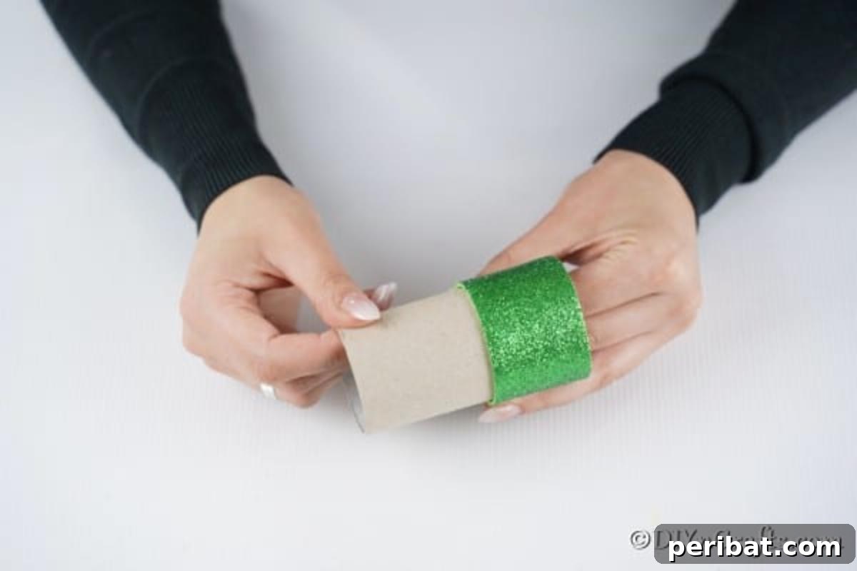 Upcycled Toilet Roll Santa Snowman and Elf for Kids 22 Securely gluing the green paper strip onto the bottom half of the toilet paper roll, forming the base of the elf decoration.