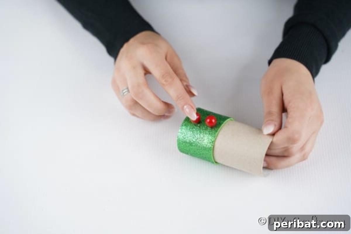 Upcycled Toilet Roll Santa Snowman and Elf for Kids 23 Affixing vibrant red buttons to the front of the green elf suit, adding a cheerful and classic detail.