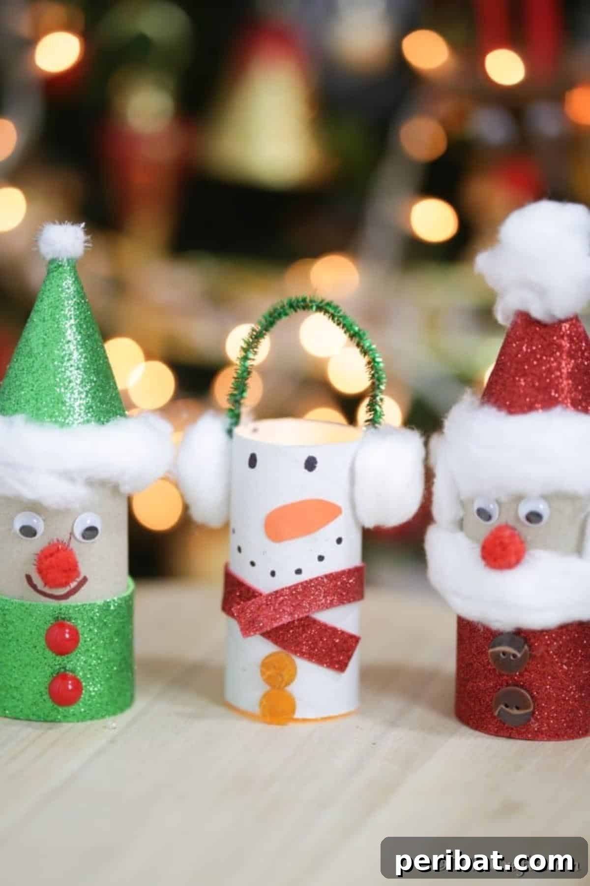 Upcycled Toilet Roll Santa Snowman and Elf for Kids 4 Three handmade toilet paper roll Christmas crafts (Santa, Snowman, Elf) displayed on a table in front of a twinkling Christmas tree.