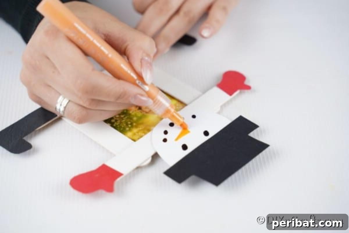 Drawing a face on a snowman craft stick photo ornament