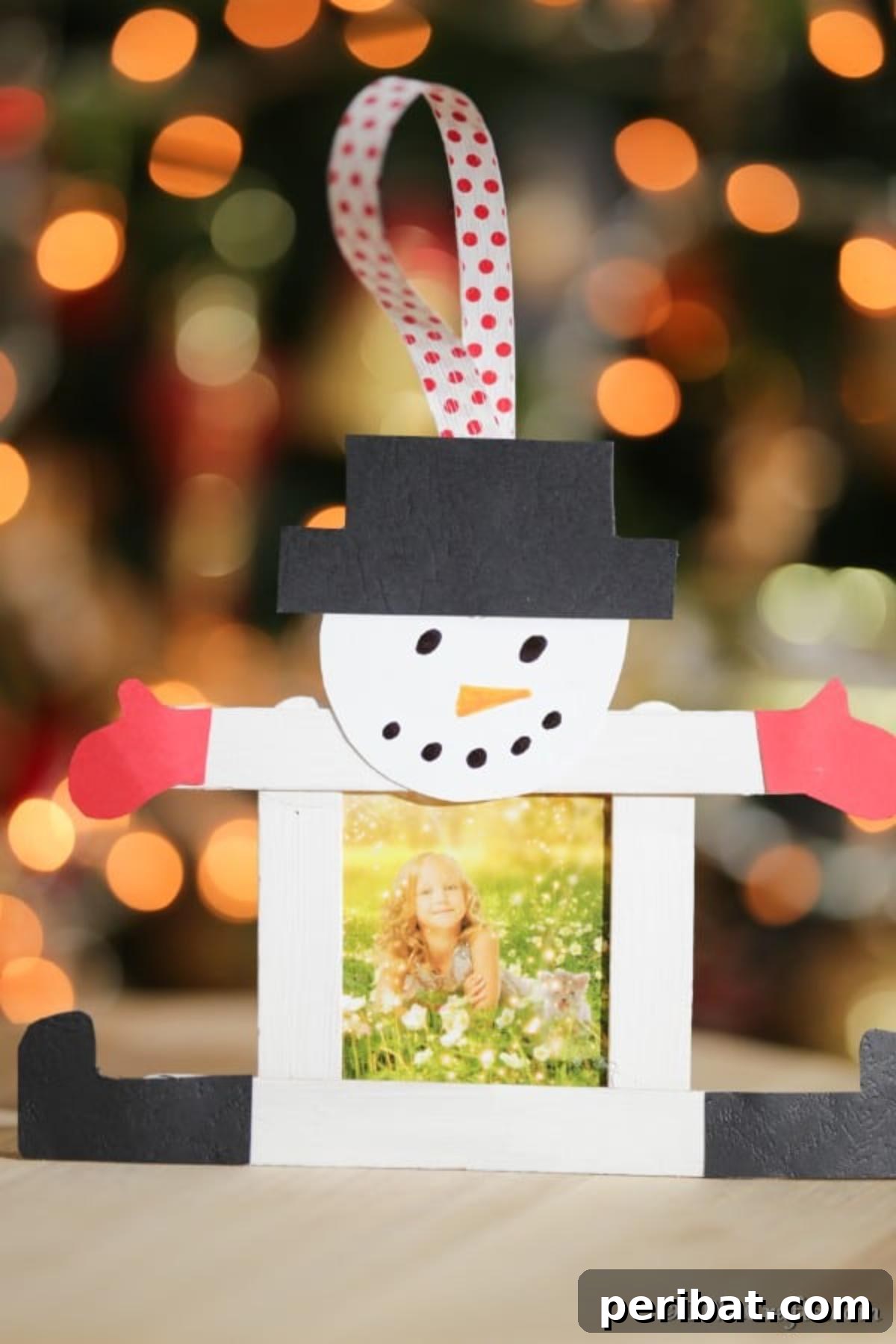 A completed craft stick snowman picture frame in front of a holiday tree