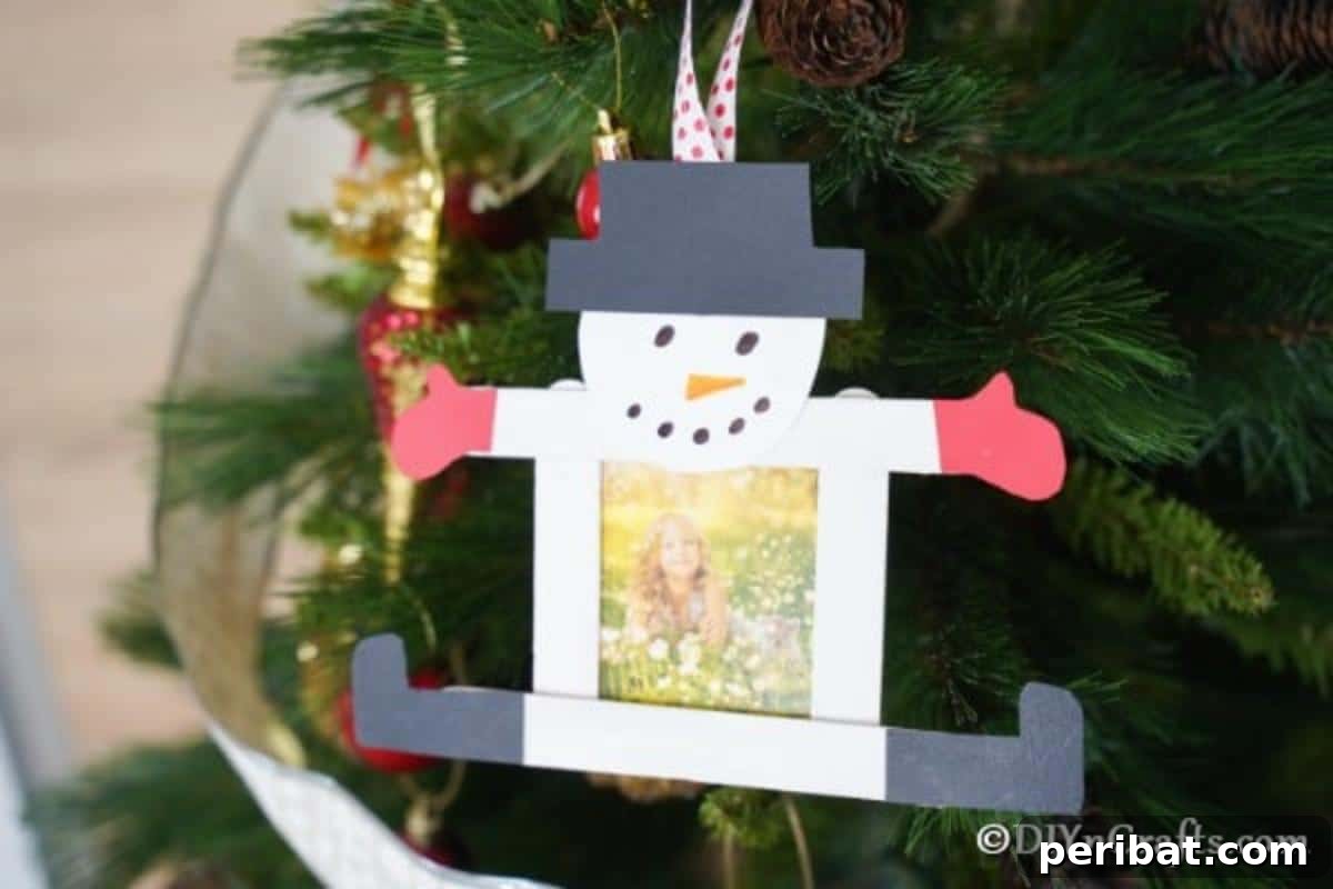 A snowman craft stick ornament hanging on a cedar Christmas tree