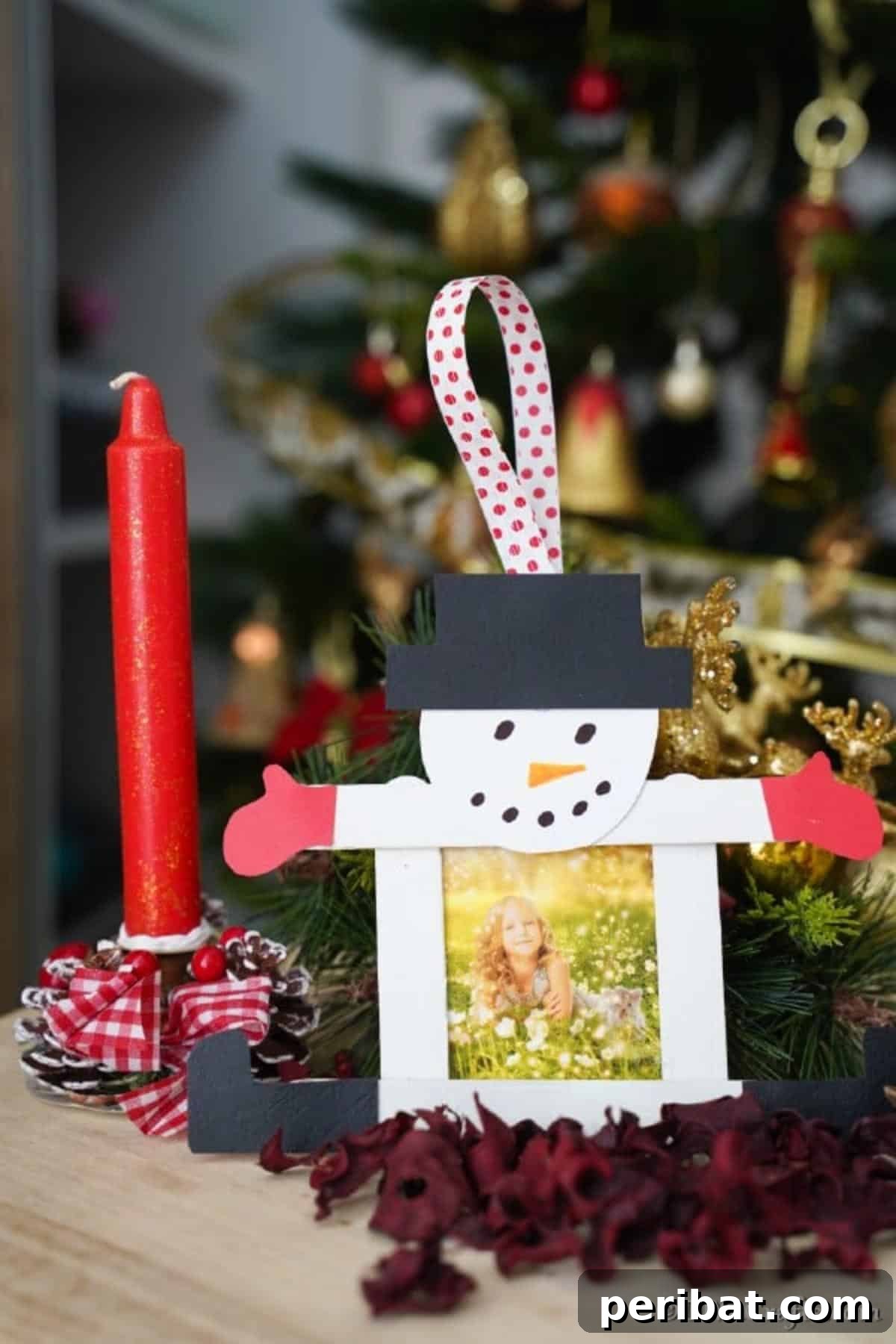 A snowman craft stick picture ornament sitting on a table next to holiday candles and wreaths