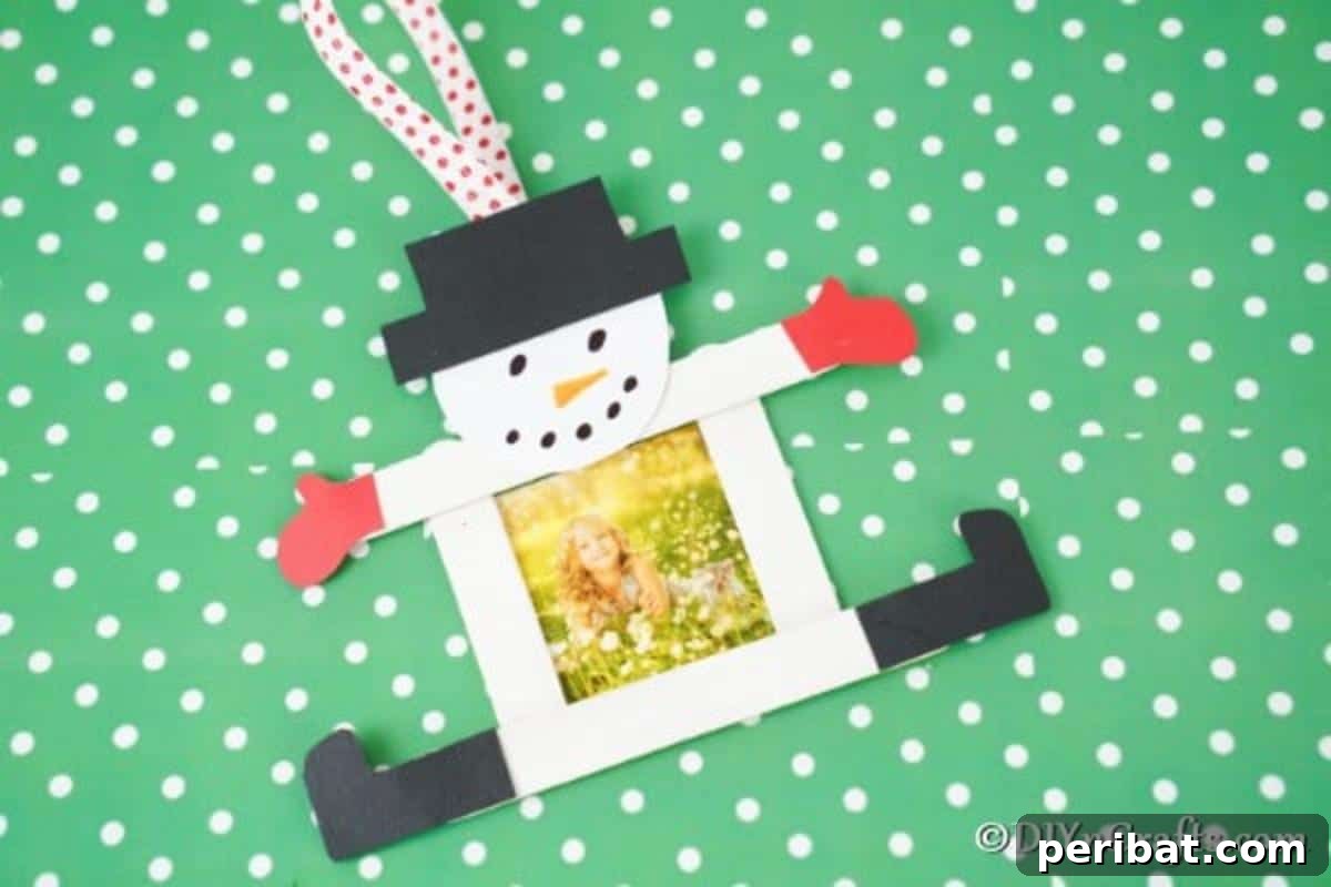 A craft stick snowman ornament laying on green and white polka dot surface