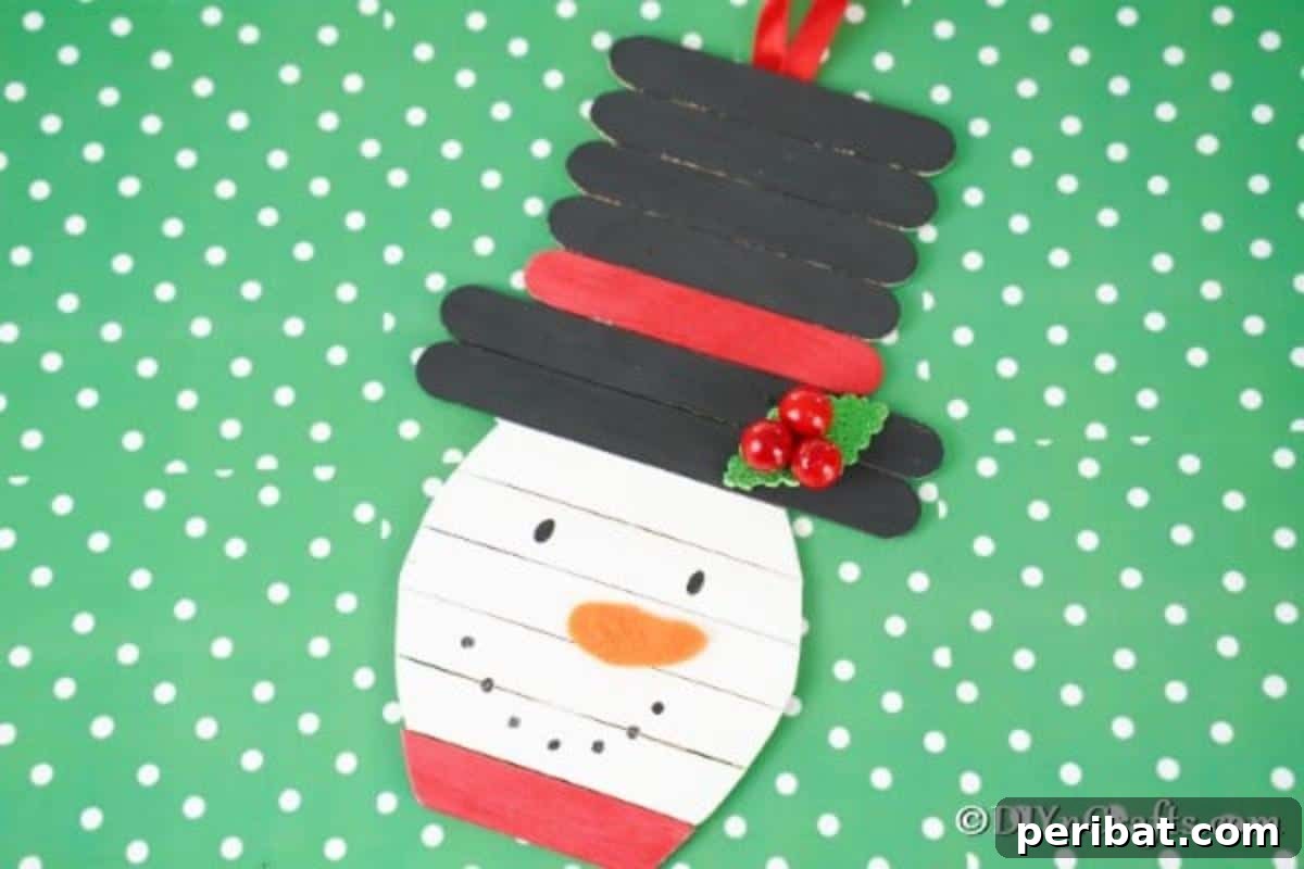 Popsicle stick snowman craft laying on green polka dot surface