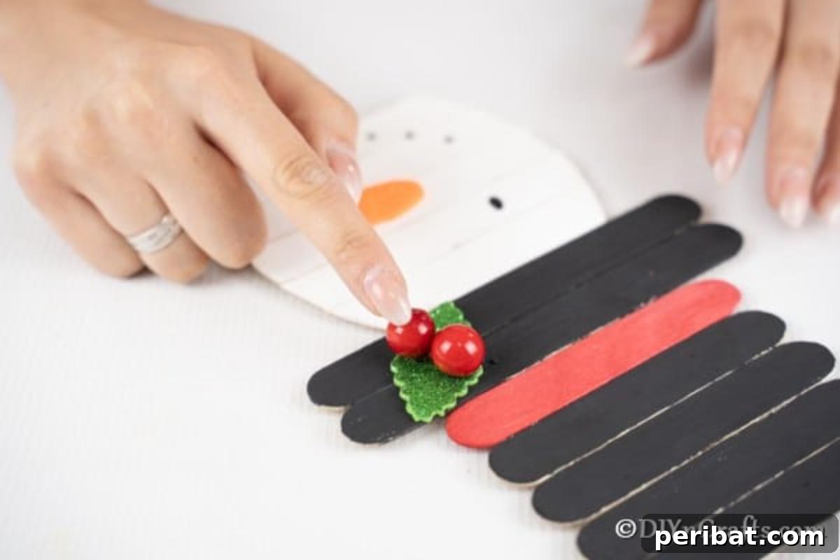 Adding the greenery and berries to the top of the craft stick snowman decoration hat. 