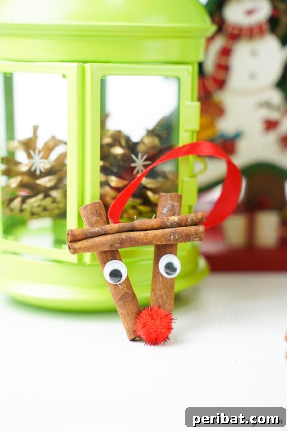 A cinnamon stick reindeer ornament leaning against a green lantern