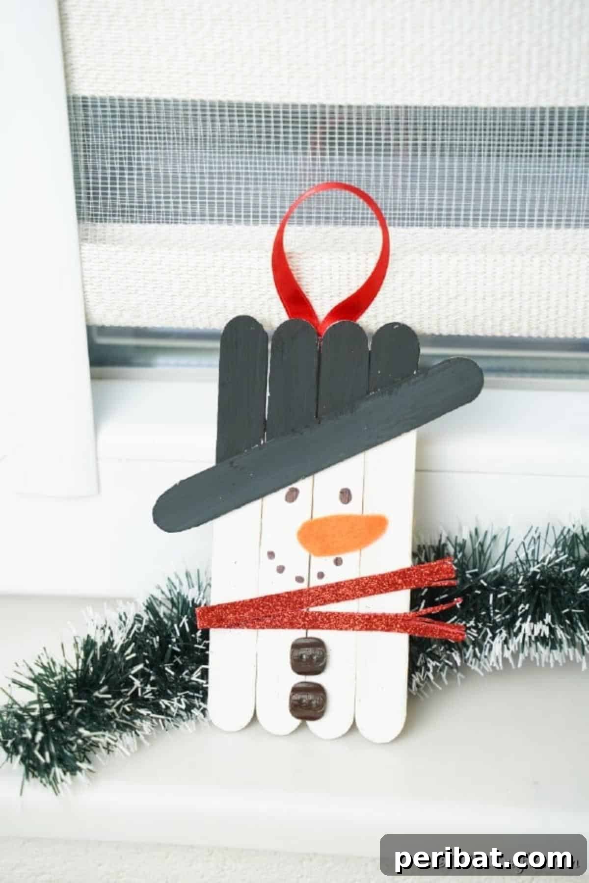 A snowman popsicle stick ornament leaned against a windowsill