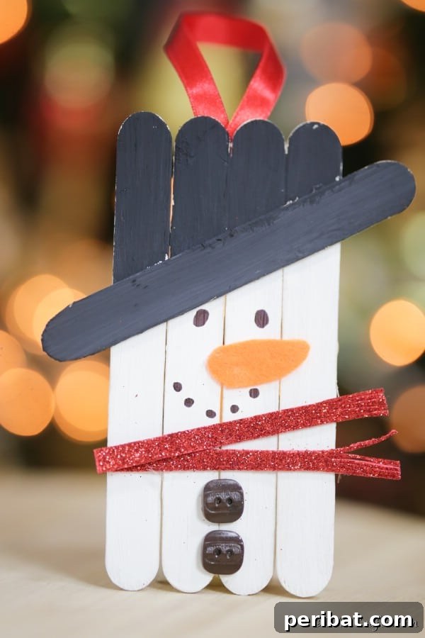 A snowman craft stick ornament displayed on a table in front of the holiday tree