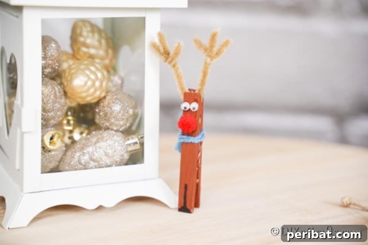 Transform Clothespins Into Adorable Reindeer Ornaments 5 The reindeer clothespin ornament sitting next to a white lantern filled with silver and gold ornaments