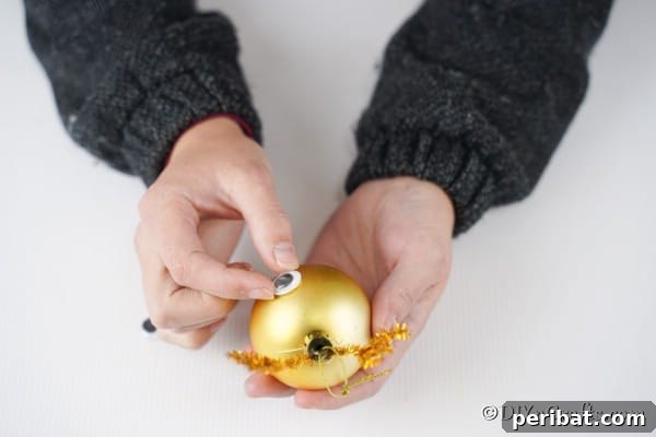 Rudolph's Dazzling Christmas Tree Bauble 15 Gluing googly eyes onto rudolf ornament, ensuring proper spacing and alignment.