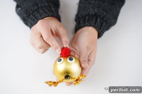 Rudolph's Dazzling Christmas Tree Bauble 16 Adding the red pom pom nose to a gold rudolf reindeer ornament, highlighting its central placement.