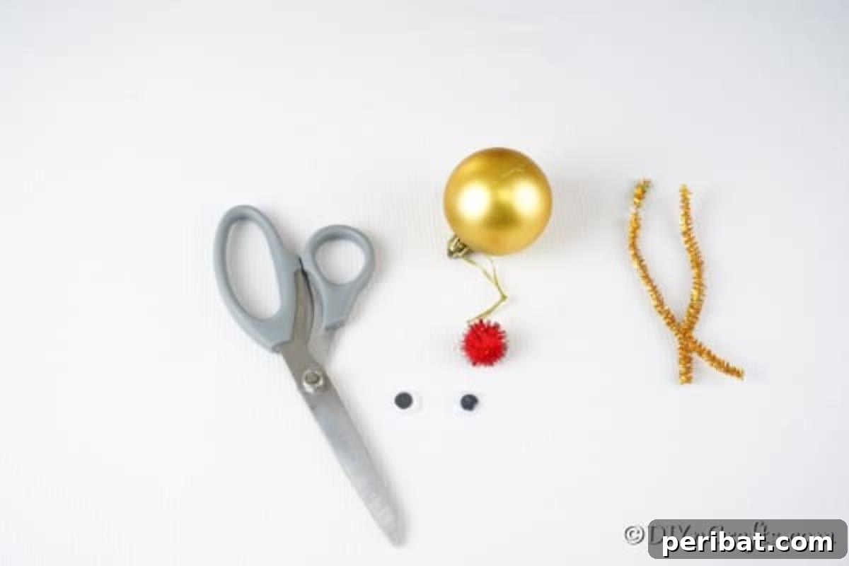 Rudolph's Dazzling Christmas Tree Bauble 6 Arrangement of supplies for making a reindeer Christmas ball ornament: gold ornaments, red pom-poms, googly eyes, pipe cleaners, glue gun, and scissors, neatly laid out.