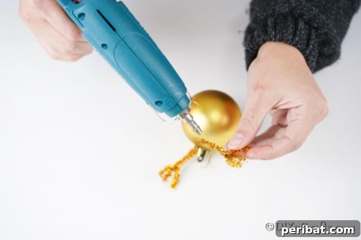 Rudolph's Dazzling Christmas Tree Bauble 8 Clearly showing the process of gluing pipe cleaner antlers on the top of a gold Christmas ornament, with placement next to the hanger.