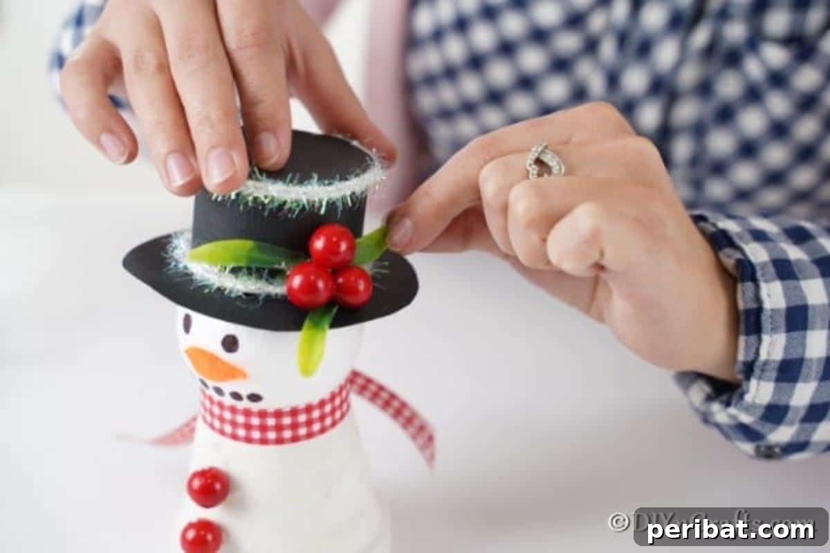 Attaching leaves and berries to top of snowman decoration
