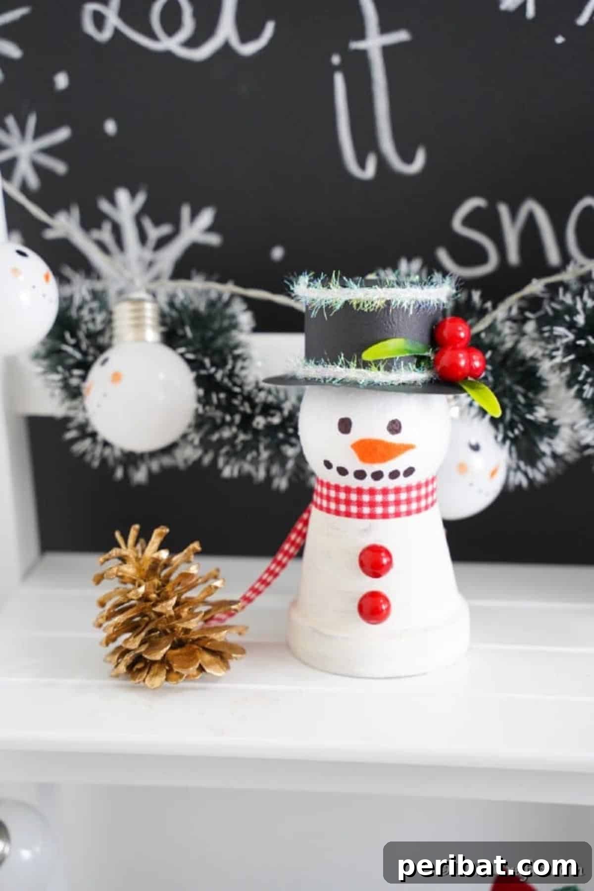 Clay pot snowman decoration on a white shelf in front of chalkboard let it snow sign
