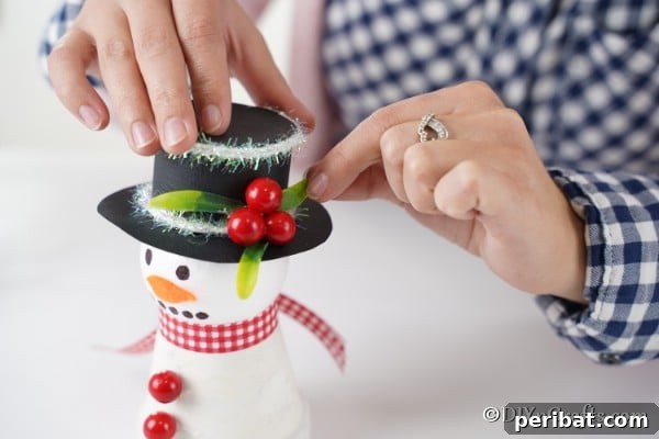Attaching leaves and berries to top of snowman decoration
