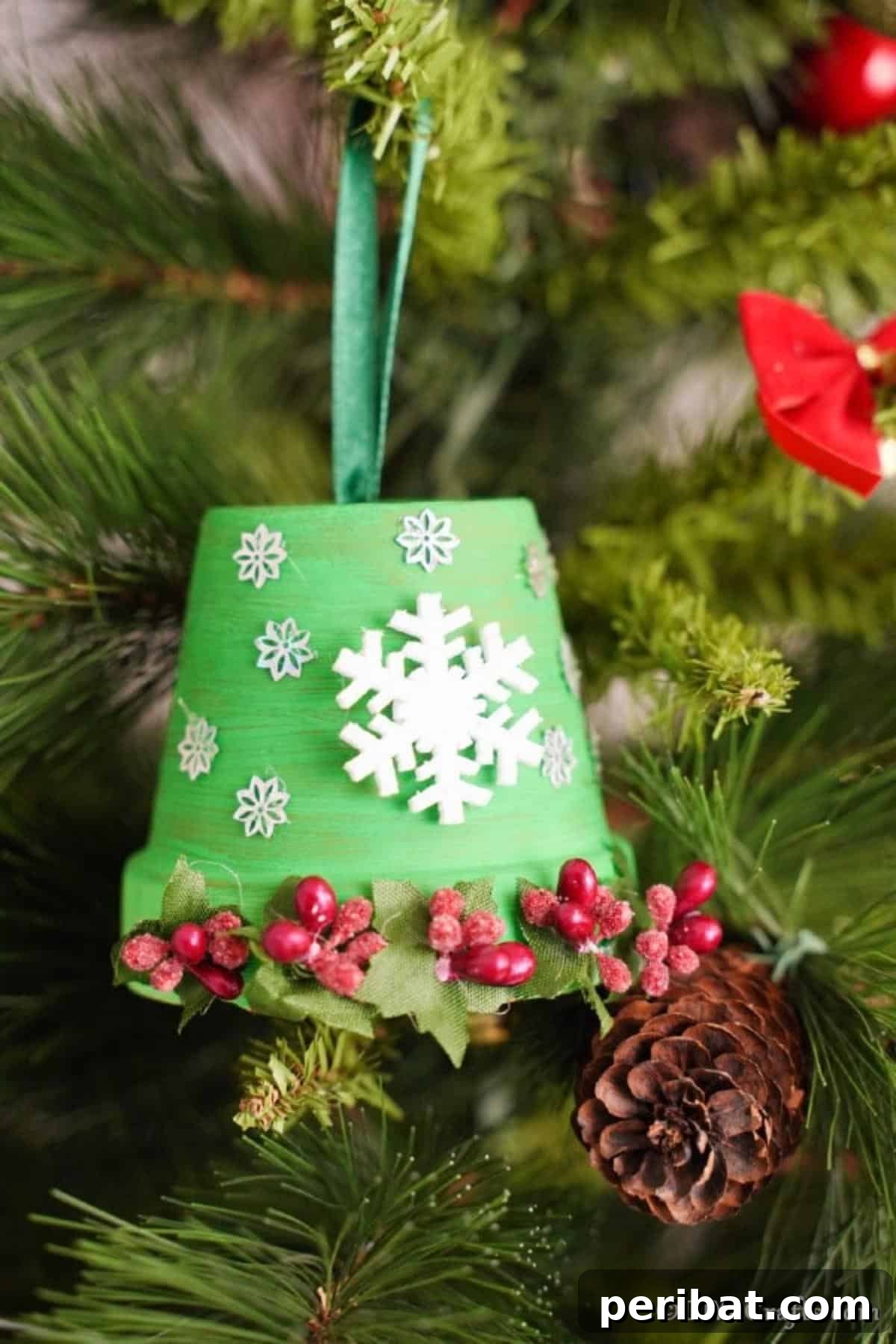 Craft Your Own Adorable Christmas Bell Ornaments 13 A charming DIY Christmas bell decoration, made from a green painted clay pot adorned with white snowflakes and red berries, hanging gracefully in a Christmas tree