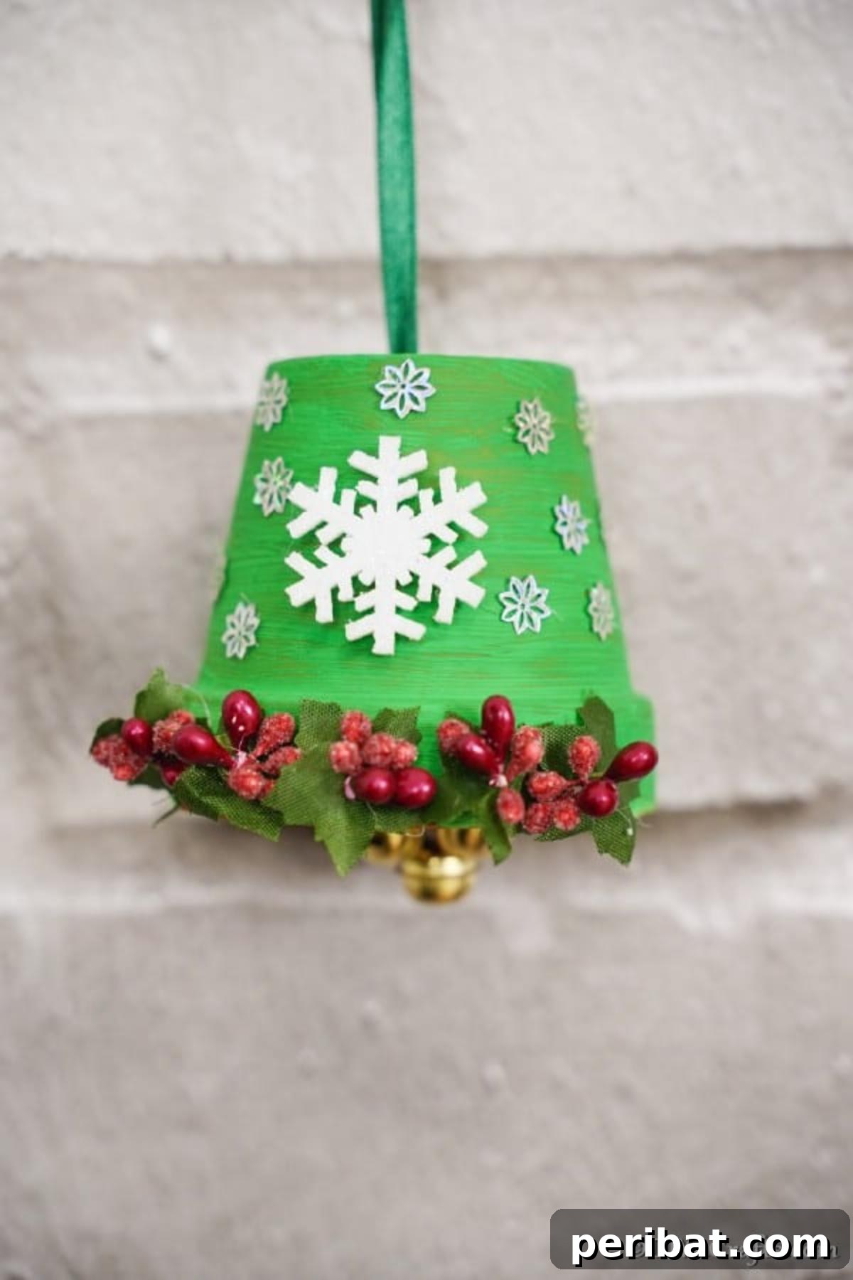 Craft Your Own Adorable Christmas Bell Ornaments 4 A charming DIY Christmas Bell, adorned with snowflakes and berries, hanging against a rustic white brick wall