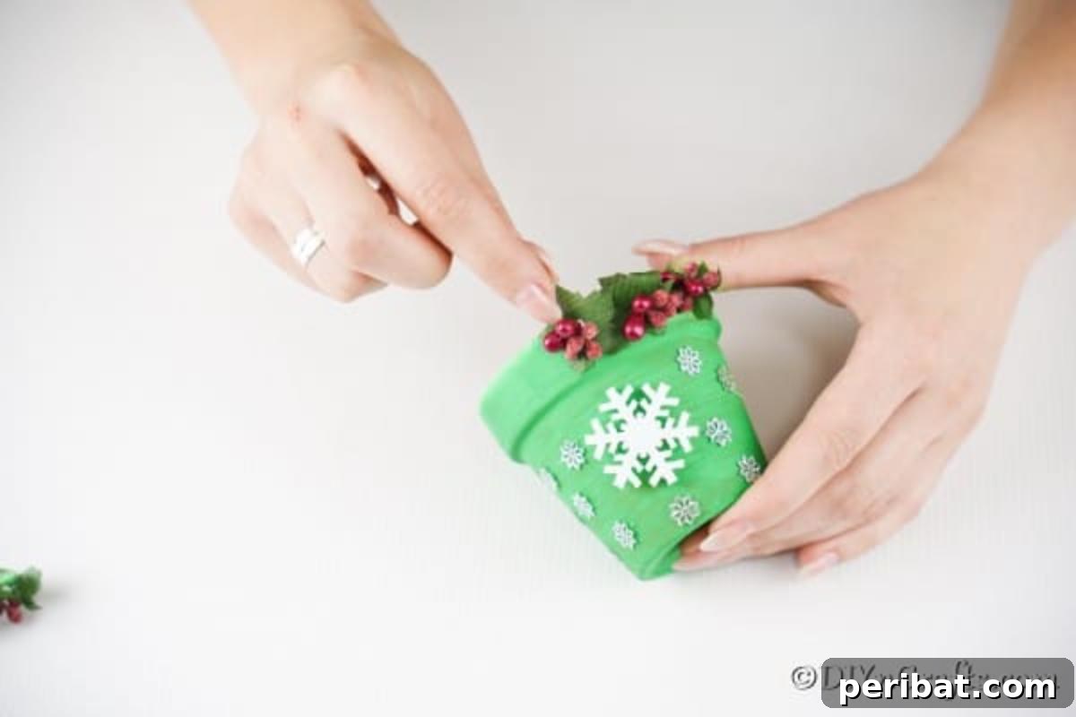 Craft Your Own Adorable Christmas Bell Ornaments 10 Gluing vibrant red artificial holiday berries and green leaves onto the bottom rim of a green painted flower pot, completing the Christmas bell decoration