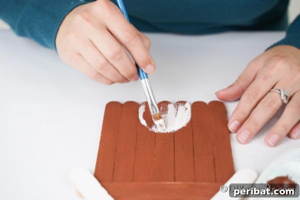 Whimsical Wooden Gingerbread House Charm 13 Painting a white door onto the brown craft stick gingerbread house decoration