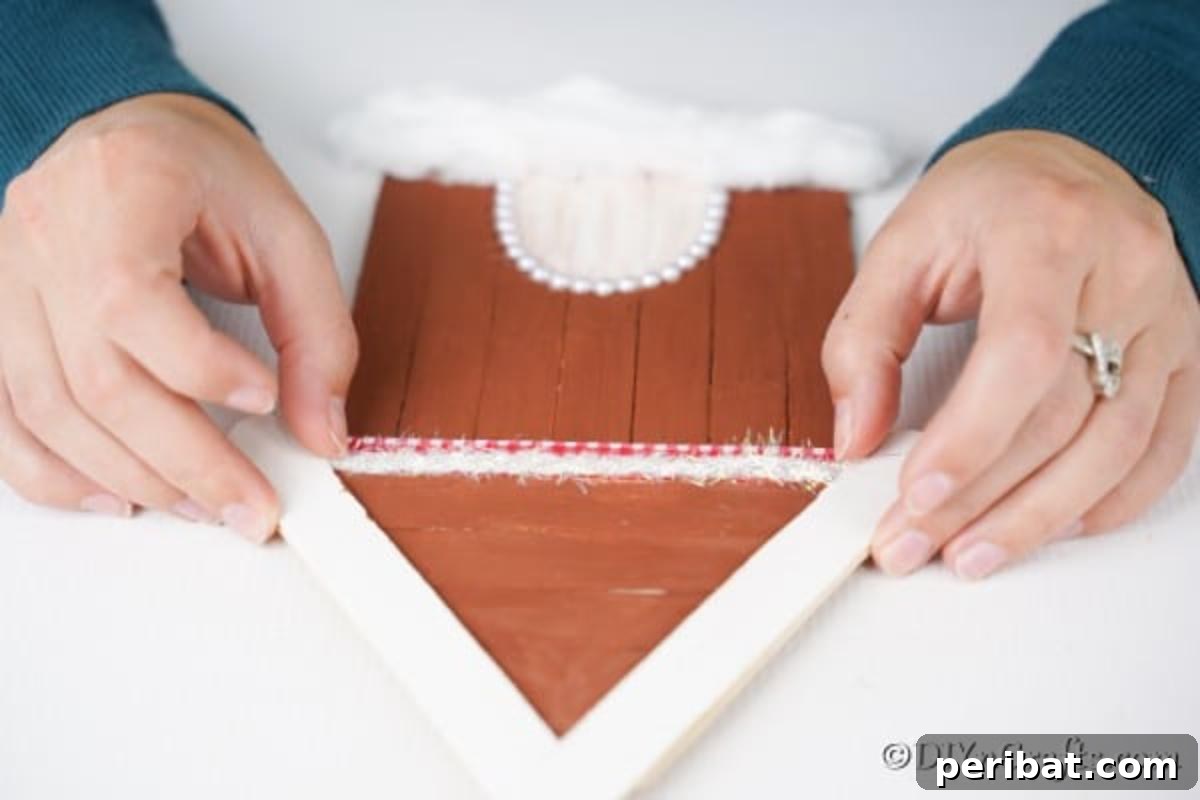 Whimsical Wooden Gingerbread House Charm 16 Adding a decorative ribbon to the roofline of the craft stick gingerbread house