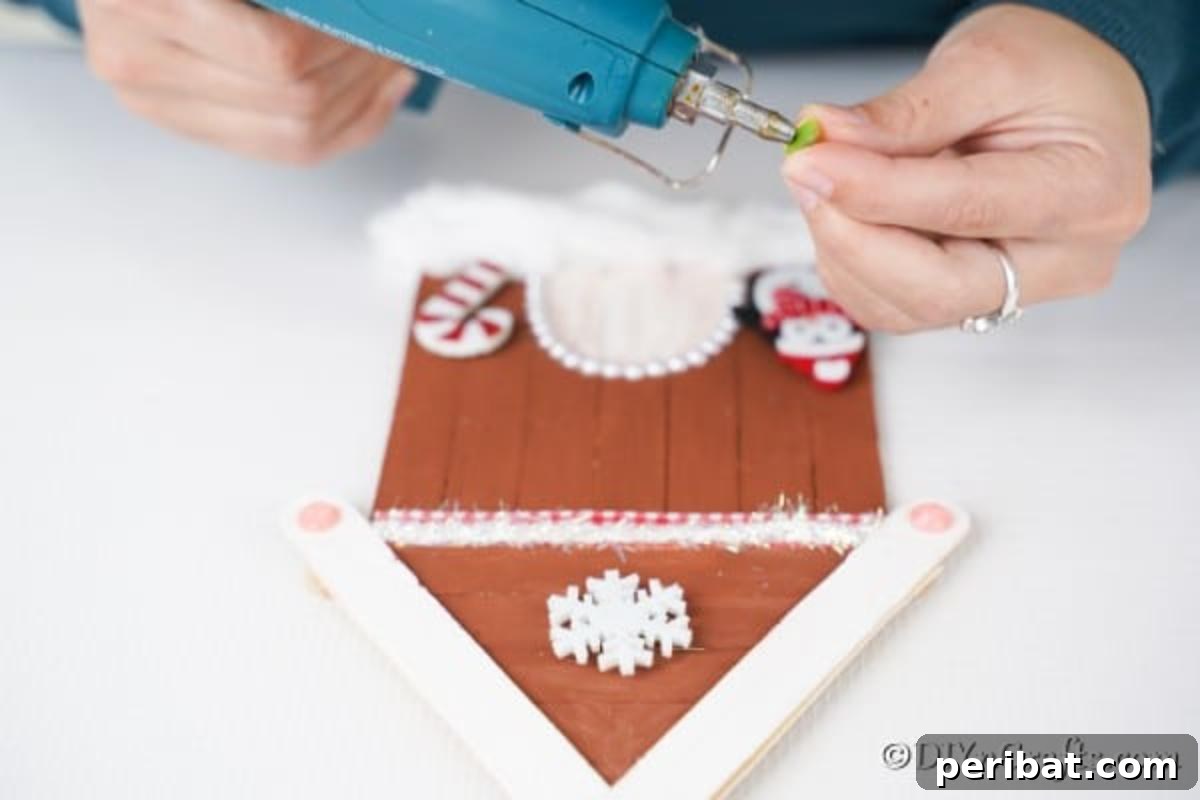 Whimsical Wooden Gingerbread House Charm 17 Gluing larger embellishments like candy canes and penguins to the front of the gingerbread house ornament craft