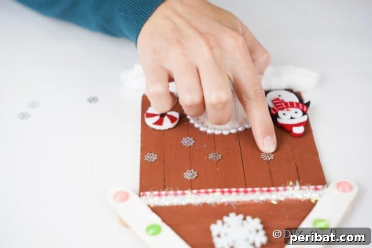 Whimsical Wooden Gingerbread House Charm 18 Adding various snowflake stickers and other small decorations to the front of the craft stick gingerbread house