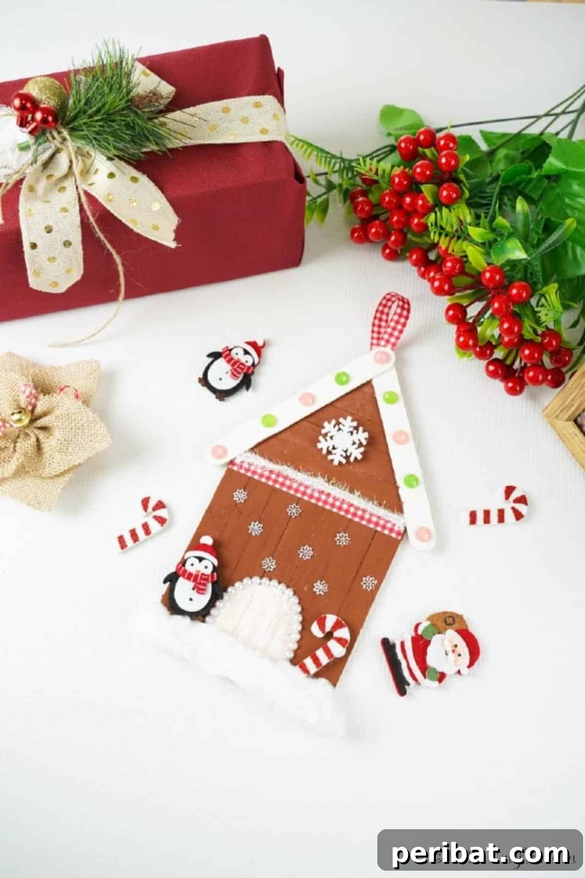 Whimsical Wooden Gingerbread House Charm 19 A finished craft stick gingerbread house ornament resting on a table surrounded by various holiday decorations