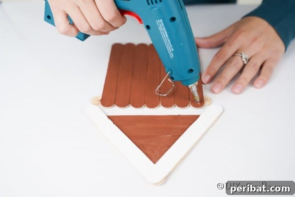 Whimsical Wooden Gingerbread House Charm 25 Gluing a roof onto the popsicle stick gingerbread house ornament